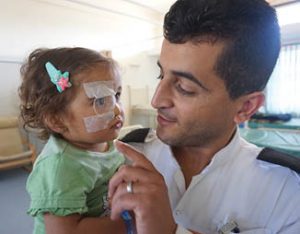 Staff nurse Ibrahim taking care of Mira, a child from Gaza who came with her grandmother for double cataract surgery. She left St John of Jerusalem Eye Hospital Group fully sighted.