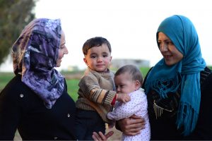 Two young refugee mothers proudly hold their toddler son and baby daughter. © Radek Procyk | Dreamstime.com.