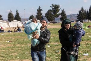 Mother and father walking through a refugee camp carrying their toddler and baby. © Vasilis Ververidis | 123rf.com.